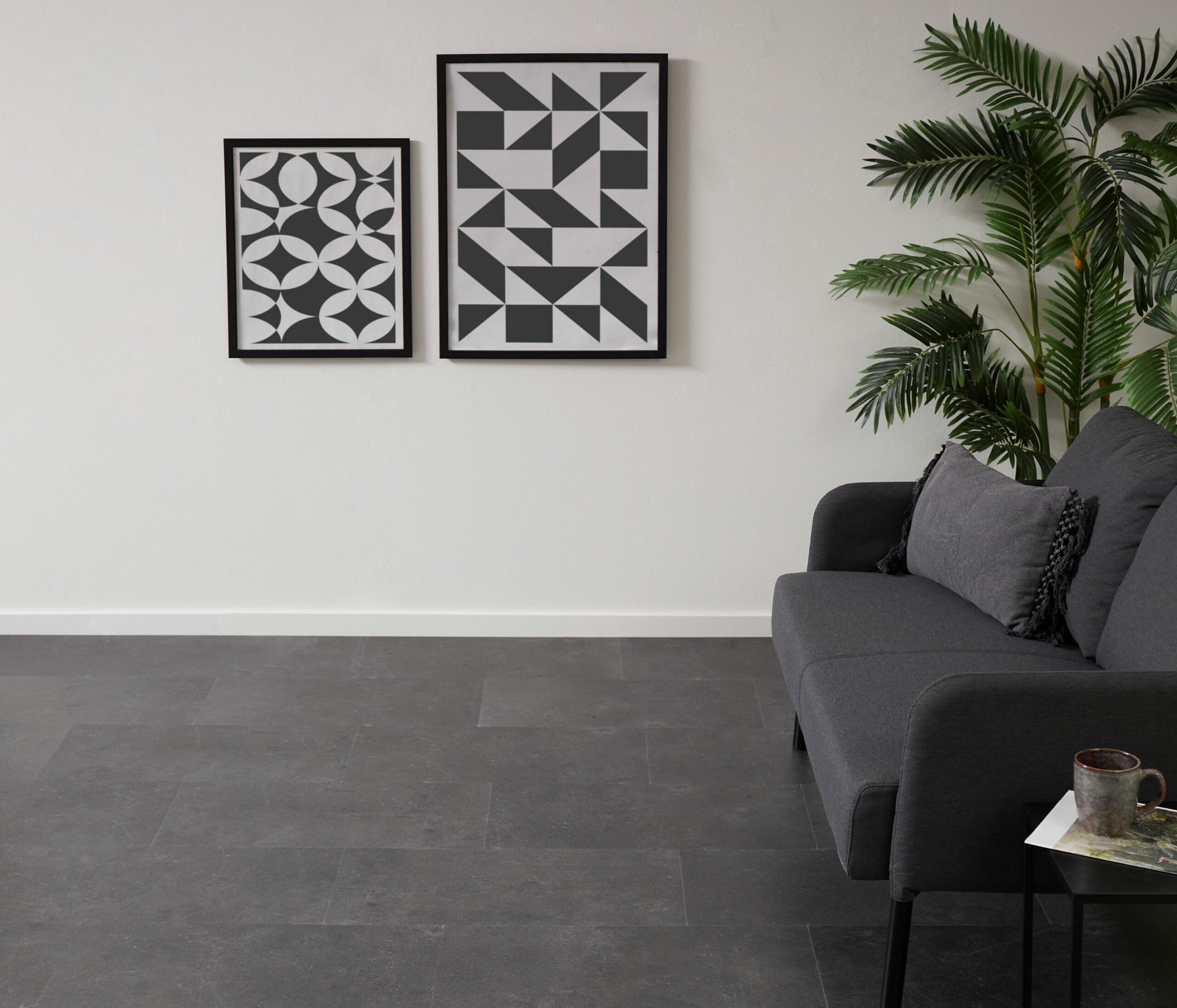 Andiamo Stone Vinylboden in dunkler Steinoptik mit einem grauem Sofa, Pflanze und moderner Wanddekoration